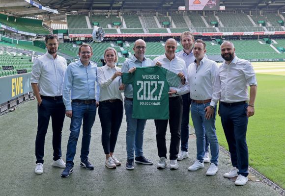 Goldschmaus im Fußballstadion. Personen halten ein Werder-Trikot hoch.